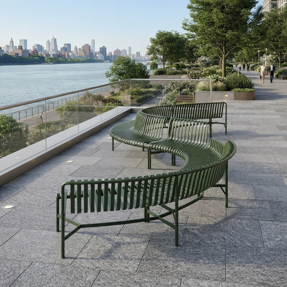 Three curved green outdoor benches arranged on a paved waterfront promenade with a river, trees, and city skyline in the background.