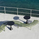 Outdoor curved lounge seating set with olive green slatted benches and round black tables on a white deck overlooking clear turquoise water.