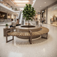 A modern curved wooden slat bench with dark metal arms arranged around a round concrete planter holding a leafy tree, set in a bright, spacious indoor shopping mall.