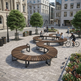 Curved wooden public benches arranged in a circular layout in a paved urban plaza, with people sitting, walking, and cycling nearby. Trees, street lamps, trash bins, and stone buildings are visible in the background.