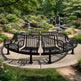 A curved black metal garden bench with a wire mesh seat and back, shown outdoors in a landscaped garden with a small pond and stone walls.