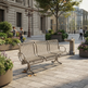 A three-seater metal park bench with a slatted wire seat and back, shown in an outdoor urban plaza with people, plants, and buildings in the background.