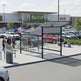 Side profile of modern shopping cart shelter featuring curved perforated roof and transparent glass enclosure.