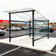 TAIMCO shopping cart shelter installed outdoors with wavy roof and glass side panels for retail cart storage.