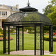 Decorative black metal gazebo in a garden setting with a house in the background