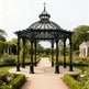 Black metal gazebo in a garden setting with pathways and greenery.