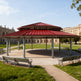 Large dodecagon two‑tier steel pavilion with red metal roof and multiple support columns