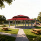 Three‑quarter view of large steel pavilion with red roof and grey columns