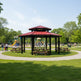 Gazebo with picnic tables in a park setting with playground equipment and trees.