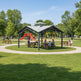Children playing on a playground with a covered picnic area in a park.