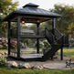 A two-tiered black metal gazebo with an attached staircase in a landscaped park setting, featuring benches, trees, and a stone pathway.