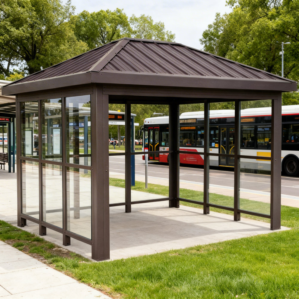 Rear angle of bus stop shelter with sloped roof and full glass back panel.