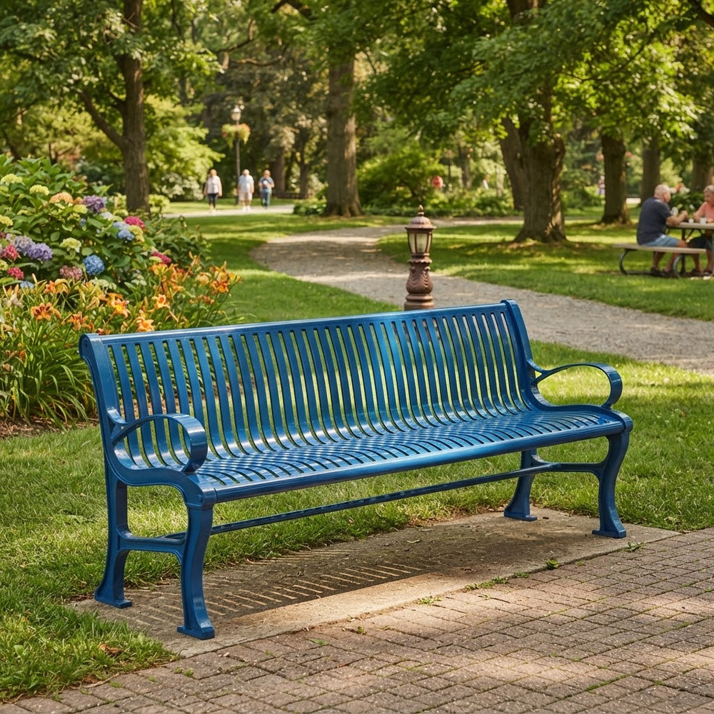 A bright blue metal park bench with slatted back and seat, situated on a paved path in a lush green park with trees, flowers, and a few people in the background.