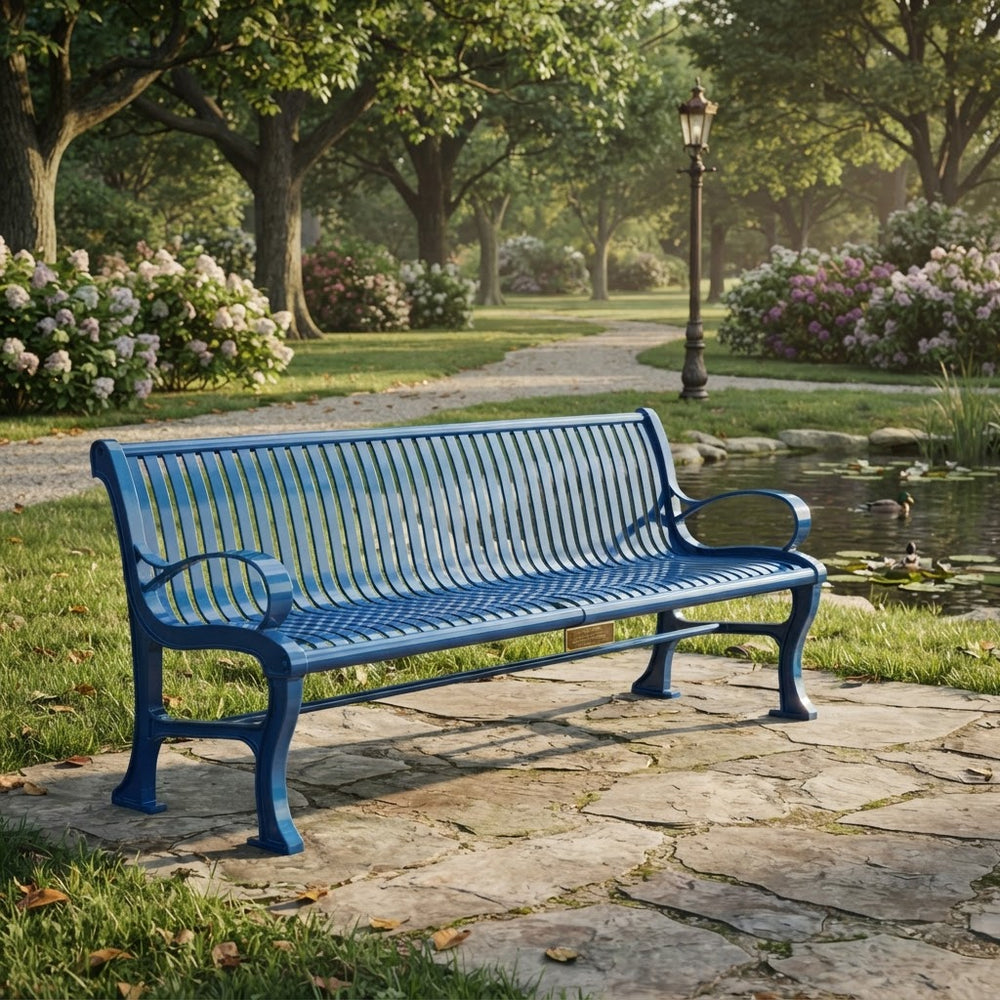A blue metal park bench with curved armrests sits on a stone path in a lush green garden with trees, flowers, and a small pond.