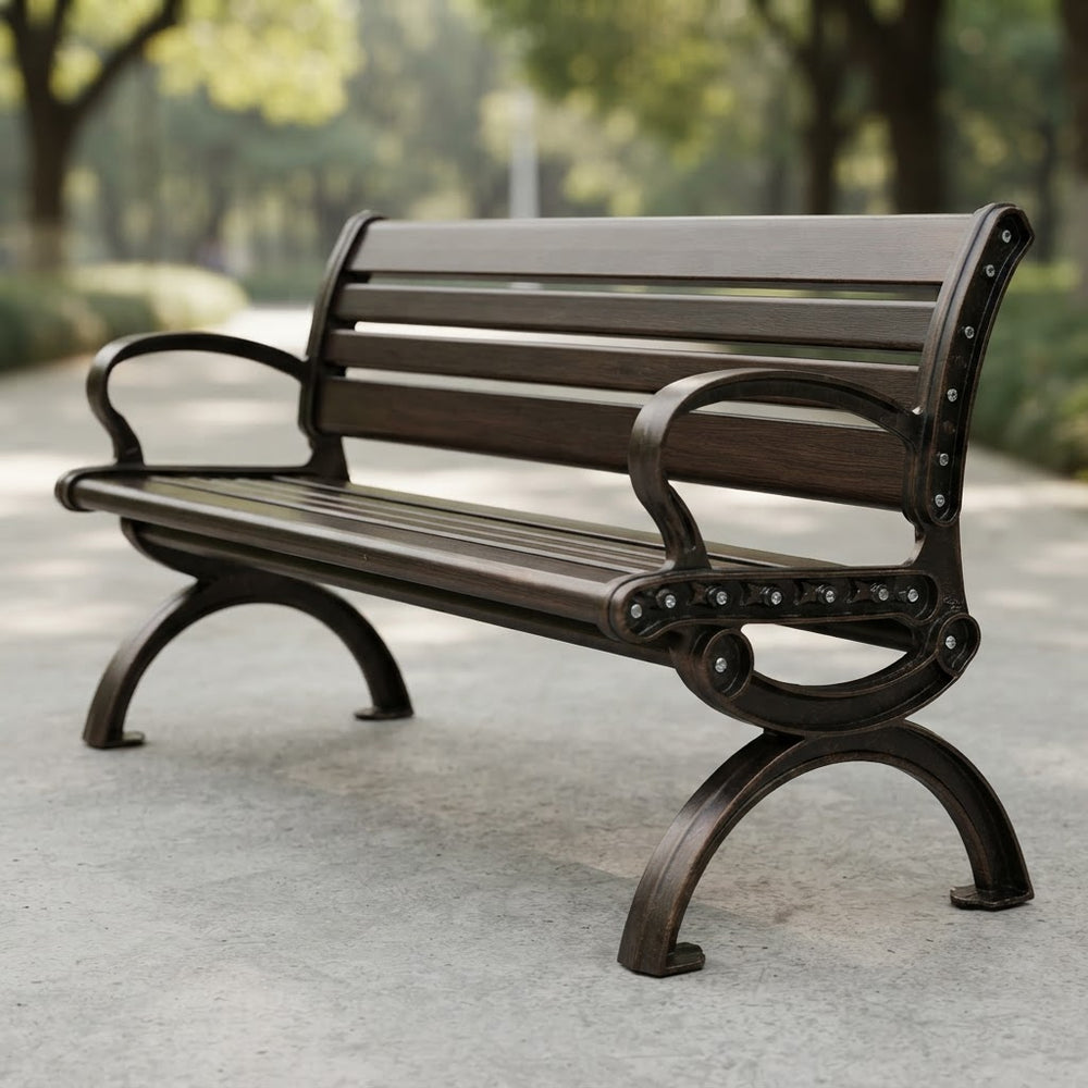 A dark brown wooden park bench with ornate metal legs and armrests, shown on a paved path in a park setting.