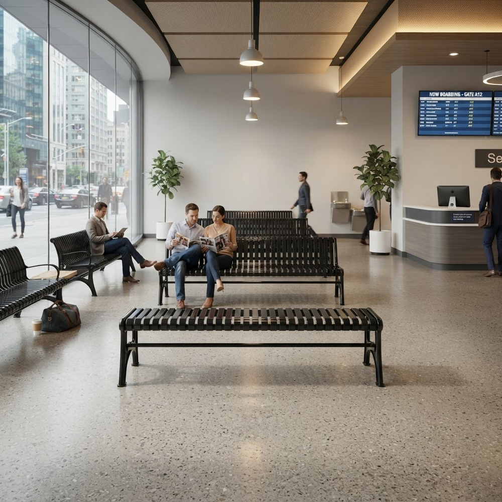 A modern, spacious airport or transit center waiting area with people sitting on black slatted benches near large floor-to-ceiling windows. The space has a polished terrazzo floor, hanging pendant lights, potted plants, a reception desk, and a departure board on the wall.