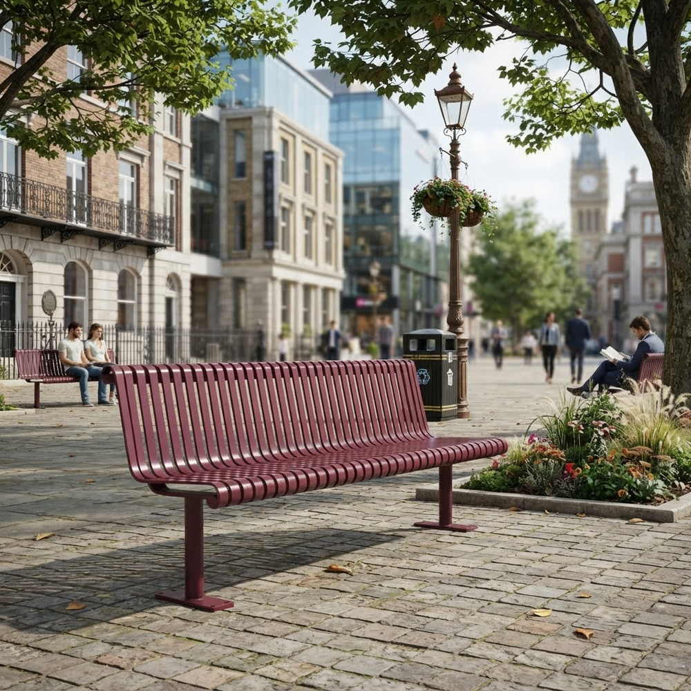 A modern outdoor park bench in a cobblestone city square, featuring a reddish-brown slatted design with a matching support post. The background shows historic brick buildings, green trees, and distant pedestrians.