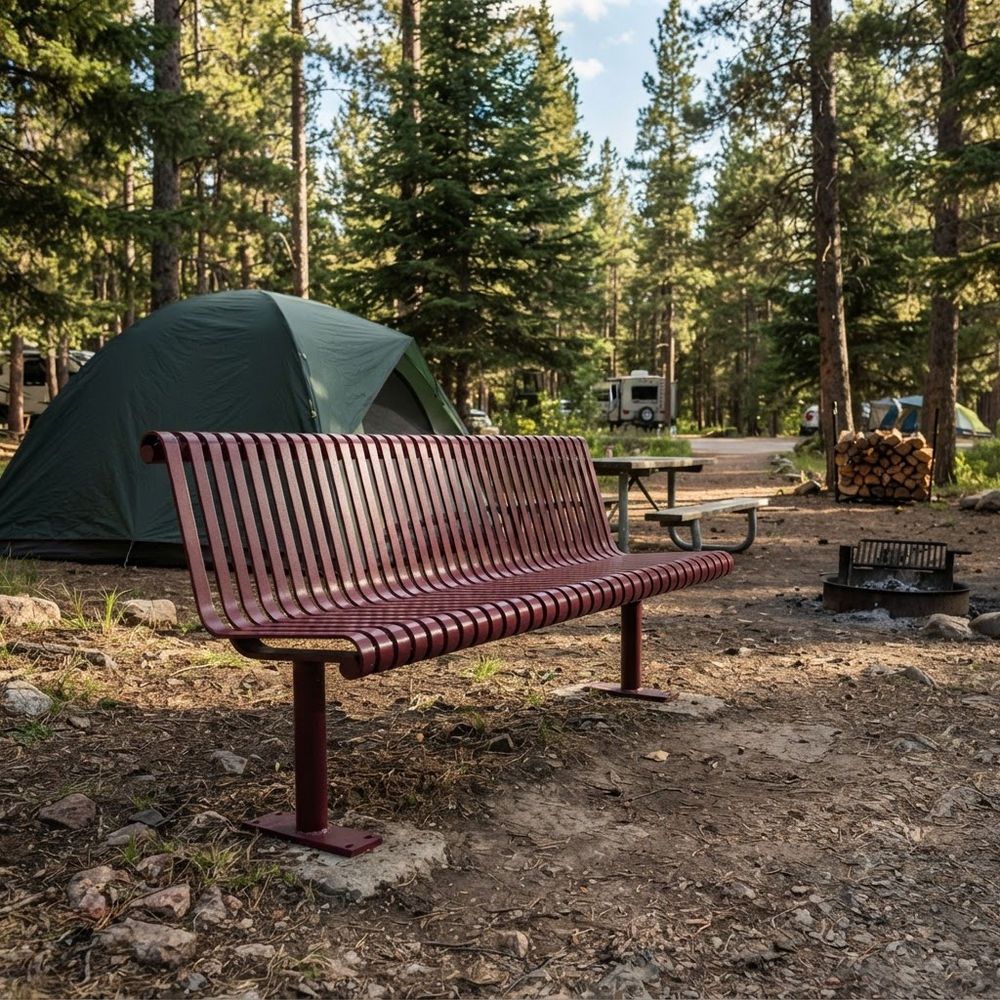 A red-brown slatted metal campsite bench in a forest clearing, with a green tent, picnic table, fire pit, and trees in the background.