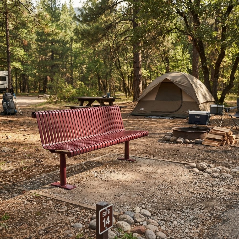 A red wooden park bench in the foreground at a forest campsite, with a beige tent, picnic table, fire pit, and trees in the background.