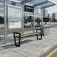 A modern outdoor bus stop shelter with a bench, a digital departure board, a transit map, and a recycling bin, shown in an urban street setting with a bus in the background.