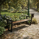 A modern outdoor bench with a light brown wooden seat and a black metal frame, situated on a stone pathway in a lush, green park with hydrangeas and trees.