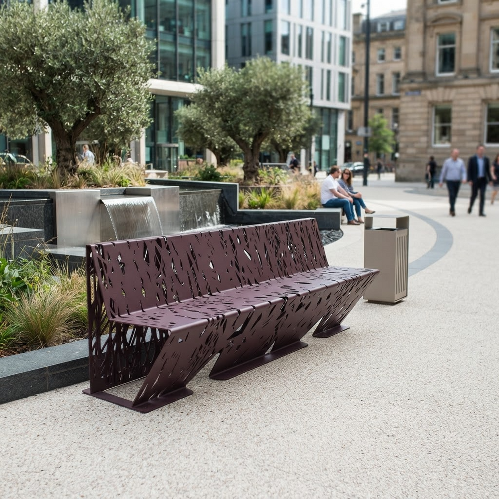A modern outdoor bench with a dark reddish-brown perforated metal design, situated in a paved urban plaza next to a stainless steel water feature and trash can.
