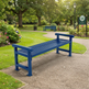 A blue slatted park bench placed on a gravel path in a landscaped garden with green grass, trees, flowers, and a signpost in the background.