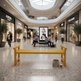 A bright yellow outdoor-style bench sits on a polished terrazzo floor in a modern, sunlit shopping mall atrium with people walking and sitting nearby. Storefronts including AURORA FASHION and TECH CAISS are visible in the background.