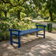 A blue wooden park bench with armrests, situated on a paved path in a lush green park with trees and flowers.
