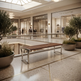A modern wooden bench with sleek silver metal legs sits on a polished terrazzo floor in a luxury shopping mall atrium, flanked by potted olive trees and glass railings.