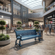 A blue wooden park bench is placed in a modern shopping mall atrium with people walking and sitting nearby, with visible Sephora and City Plaza signage in the background.