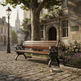 A wooden park bench with ornate black metal arms sits on a cobblestone street beside a stone building, flowers, a tree, and a street lamp in a real outdoor environment.