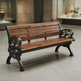 A wooden park bench with ornate black cast iron arms and legs, shown in a blurred indoor public space.