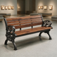 A wooden park bench with ornate black cast iron arms and legs, shown in a spacious, modern art gallery or museum interior.