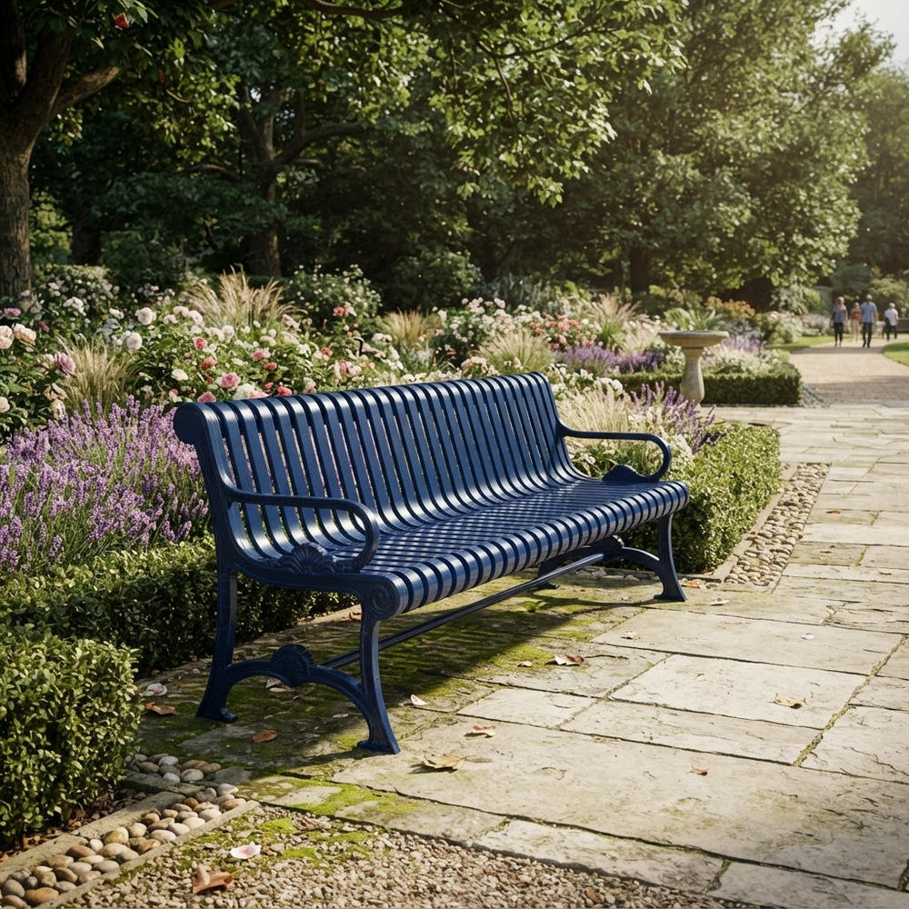 A dark blue metal park bench with a slatted back and seat, situated on a stone pathway in a lush garden with flowers and trees.