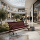 A red wooden slat bench sits in a luxury shopping mall atrium with marble floors, potted trees, and shoppers walking in the background. Visible storefront signs include Louis Vuitton, Prada, Chanel, and Apple Store.