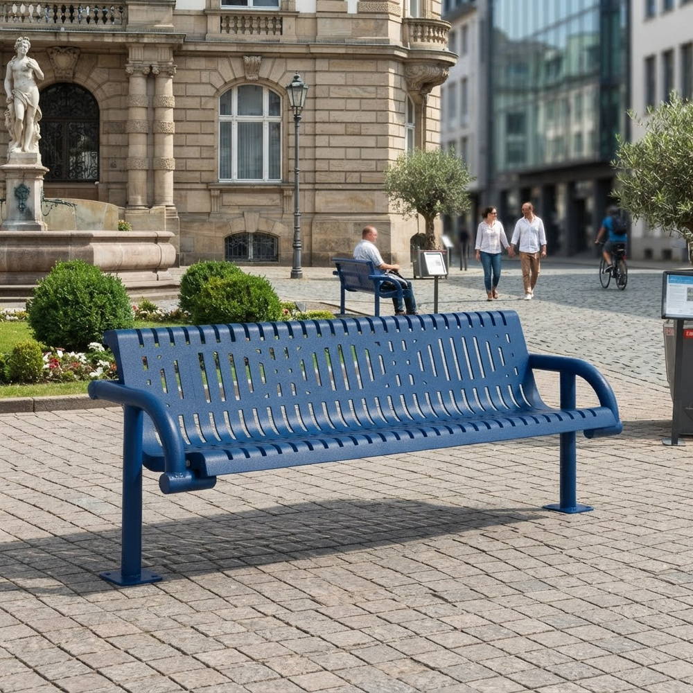 A blue metal park bench with a slatted back and seat, shown in an outdoor urban plaza with stone paving, historic buildings, pedestrians, and greenery in the background.