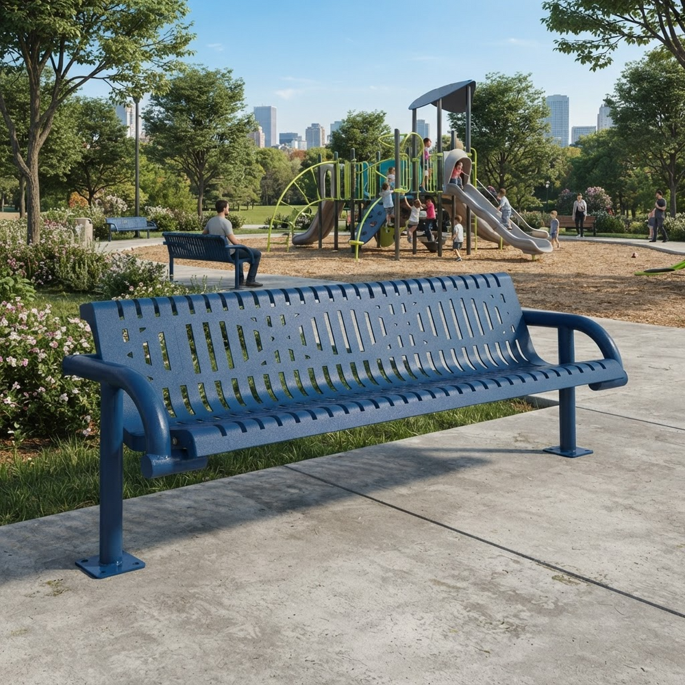A blue metal park bench with a slatted back and seat sits on a concrete path in a city park, with a playground, trees, and distant buildings in the background.
