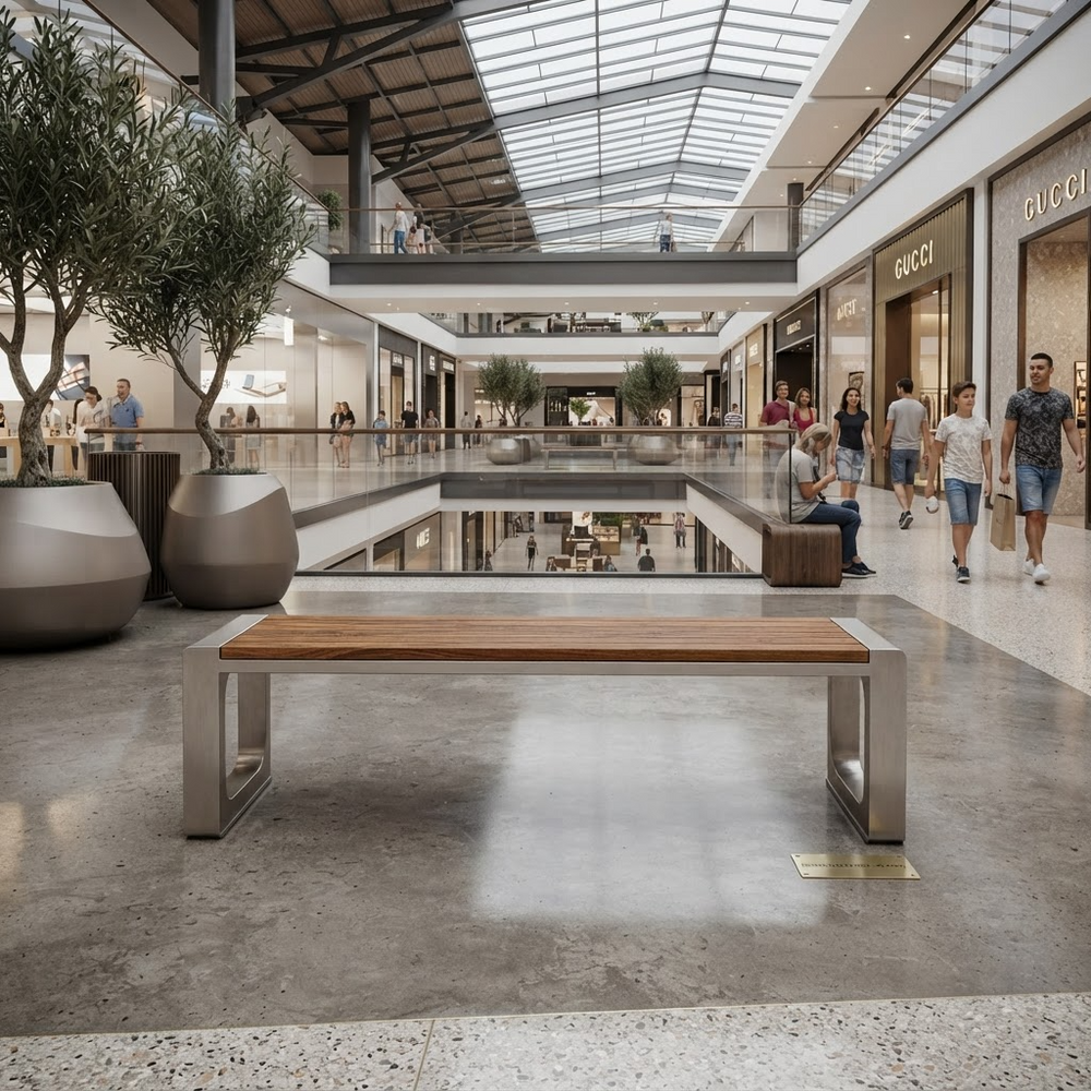 A modern wooden and metal bench in a spacious, sunlit shopping mall atrium with glass ceiling panels, water features, and shoppers walking in the background.