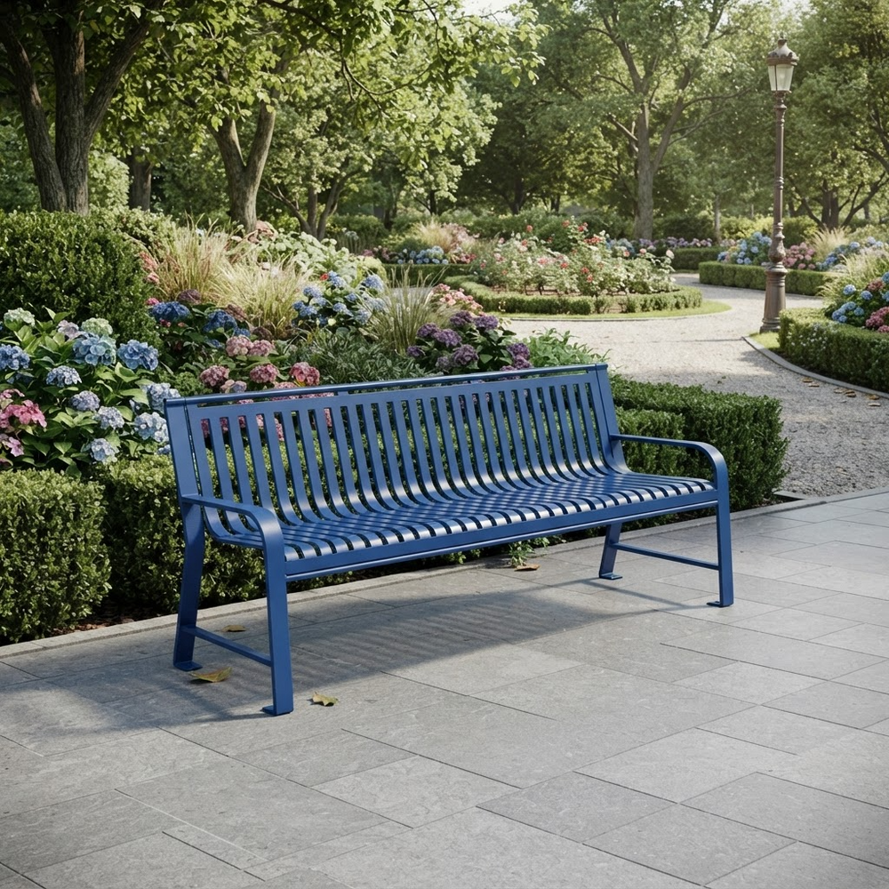 A blue metal park bench with a slatted back and seat, positioned on a paved pathway in a lush, green garden with flowers and trees in the background.
