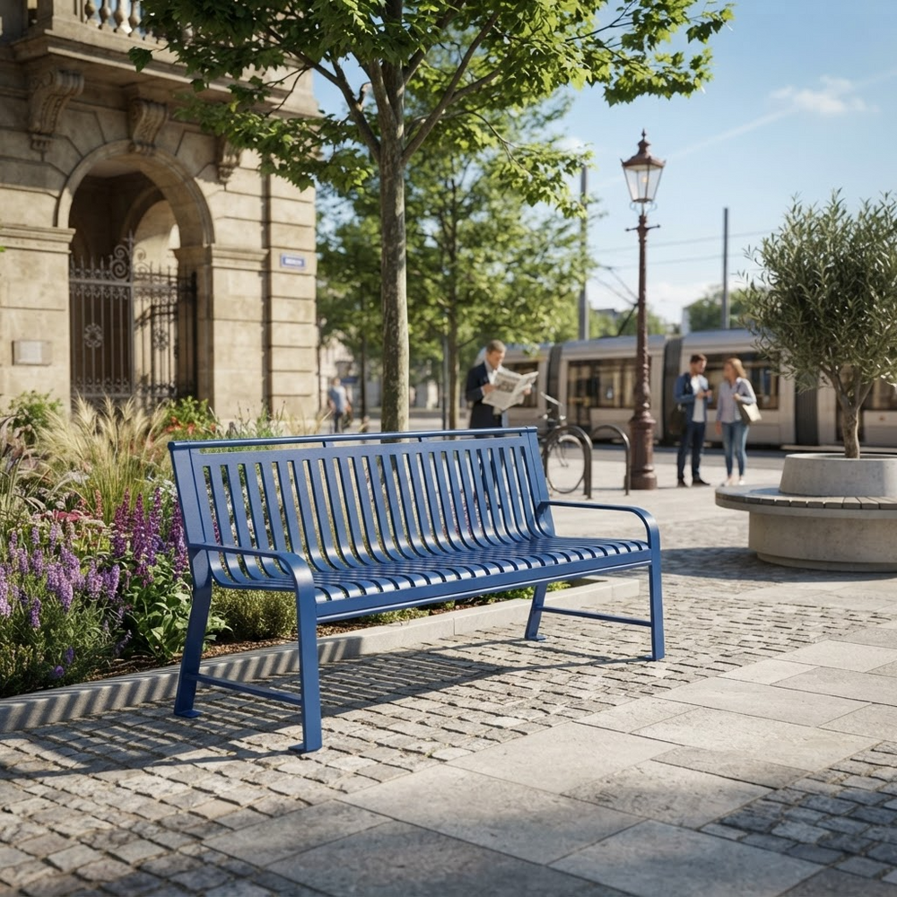 A blue metal park bench with a slatted back and seat, positioned on a cobblestone plaza in an outdoor urban setting with trees, a stone building, and people in the background.