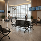 Airport terminal interior with black metal waiting benches, large floor-to-ceiling windows, departure boards, and several people seated or standing in the space.