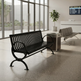 A black metal slatted waiting room bench with curved armrests is shown in a modern indoor terminal or lobby setting with large windows, a potted plant, a trash can, and another seating area in the background.