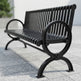 A black metal park bench with a slatted back and seat, shown outdoors on a light gray paved surface with a blurred background.