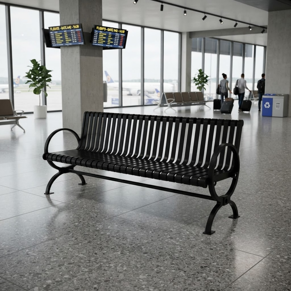 A black metal airport bench with a slatted back and seat, positioned in a spacious, modern airport terminal with large windows, flight information boards, and travelers in the background.