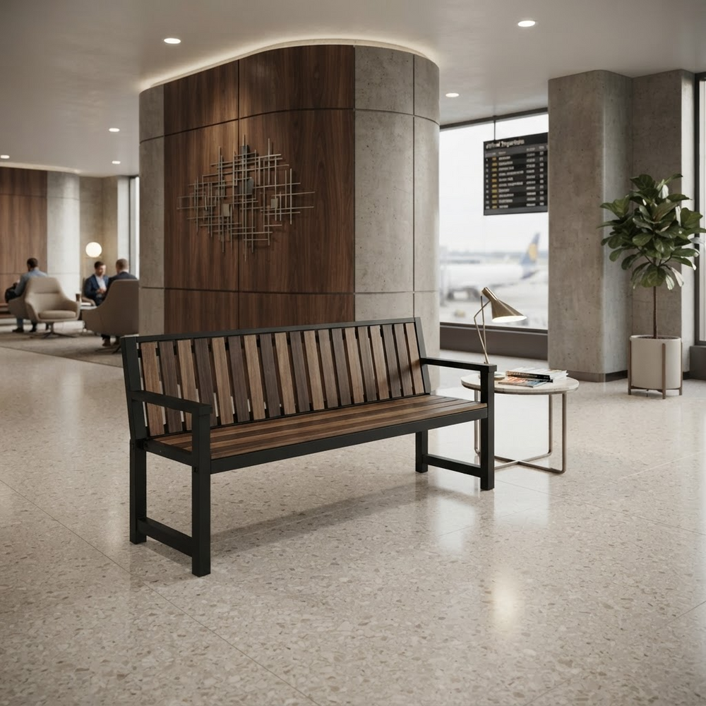 A modern wooden slat bench with a black metal frame sits in a spacious airport terminal lounge. The bench has a warm medium-brown wood seat and back slats with black armrests and legs.