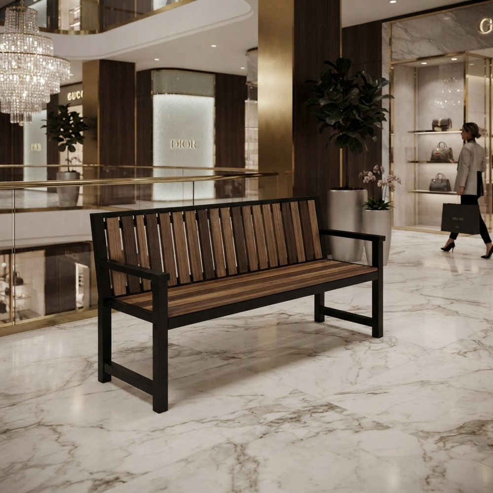 A modern wooden slat bench with a black metal frame sits on a polished marble floor in a luxury shopping mall interior. A person carrying a Dior bag walks in the background near glass display cases and potted plants.