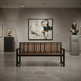 A modern wooden slat bench with a black metal frame is centered in a minimalist gallery space with a gray concrete floor, a large abstract painting on the wall, and bronze busts on display pedestals.