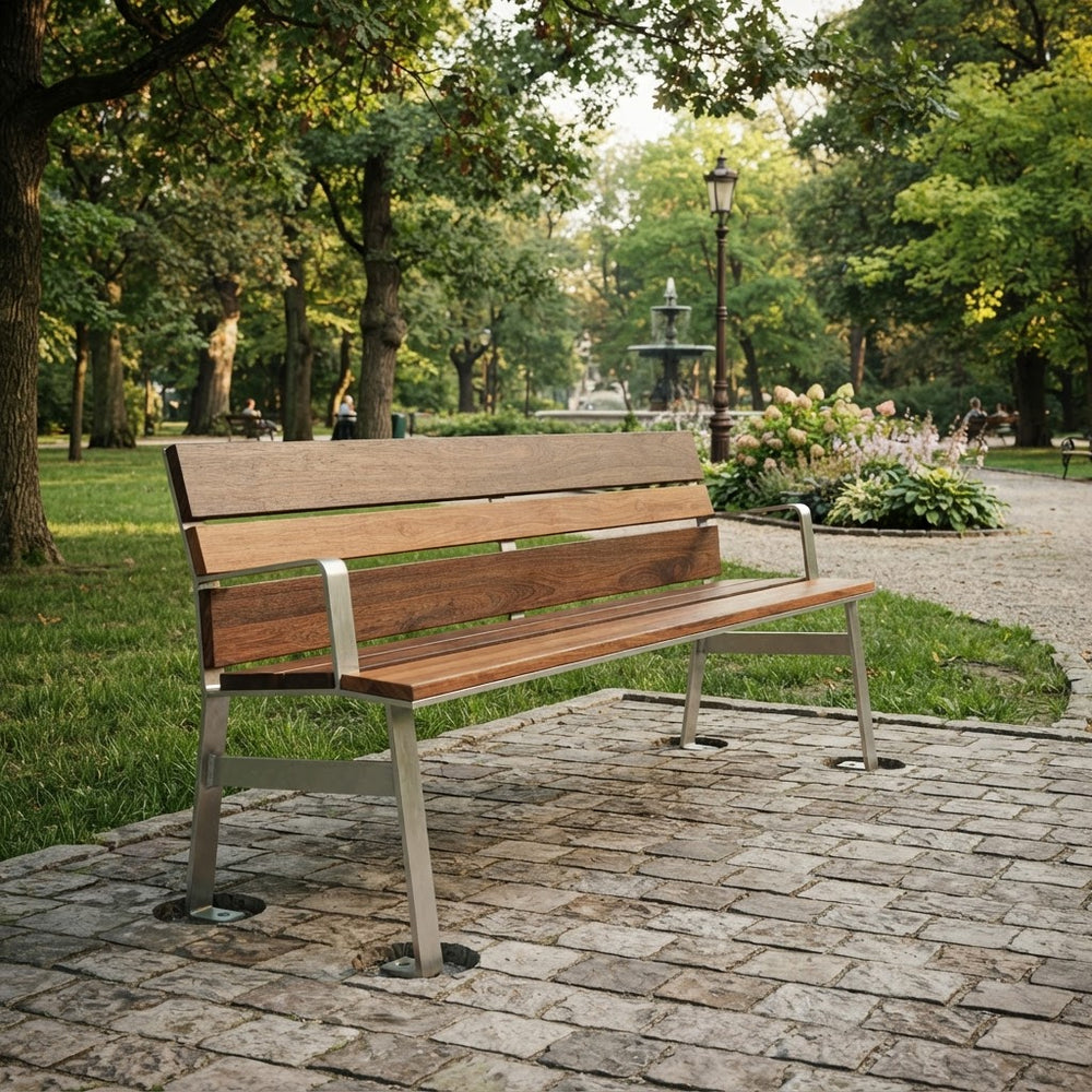 A modern wooden park bench with a brown wood-grain seat and backrest, supported by a silver metal frame, situated on a stone paved path in a lush green park.