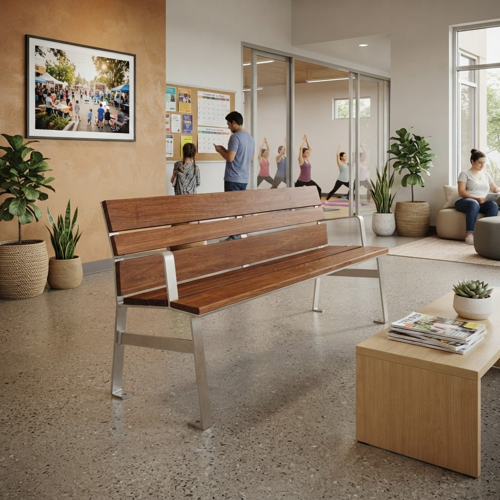 A modern wooden bench with a brushed silver metal frame is shown in a bright, contemporary indoor public space with people, plants, and a coffee table in the foreground.